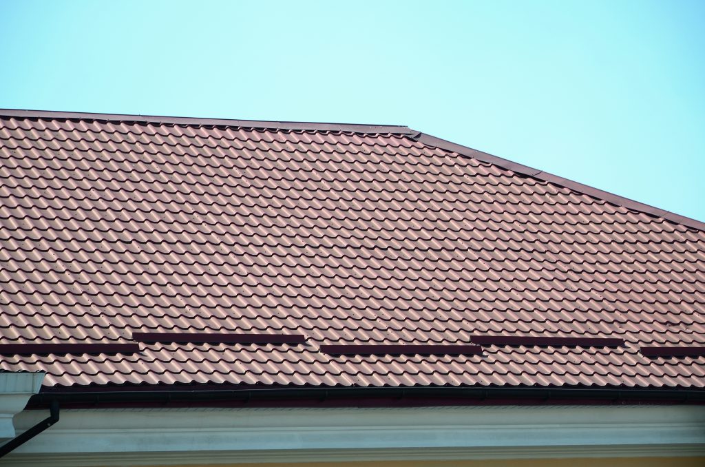A fragment of a roof from a metal tile of dark red color. Quality Roofing