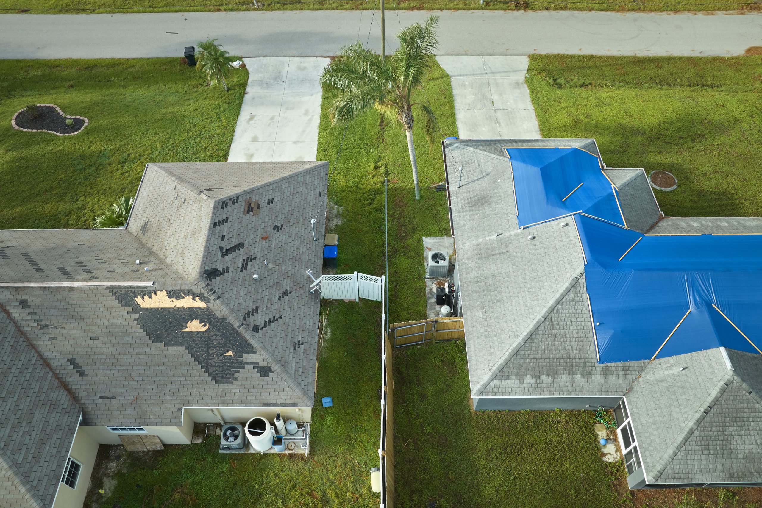Top view of leaking house roof covered with protective tarp sheets against rain water leaks until replacement of asphalt shingles. Damage of building rooftop as aftermath of hurricane Ian in Florida